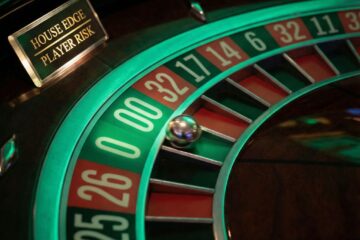 초록색 제로와 더블 제로 포켓이 두드러지게 빛나는 룰렛 휠의 클로즈업으로, 카지노의 우위와 플레이어의